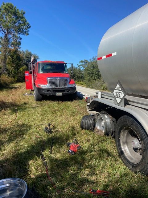 Red fire truck and tanker truck on a grassy roadside under a blue sky.