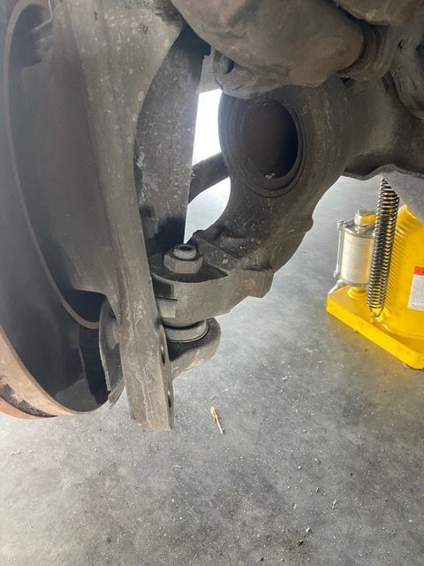 Car suspension components, including a control arm and wheel hub, with a jack visible.