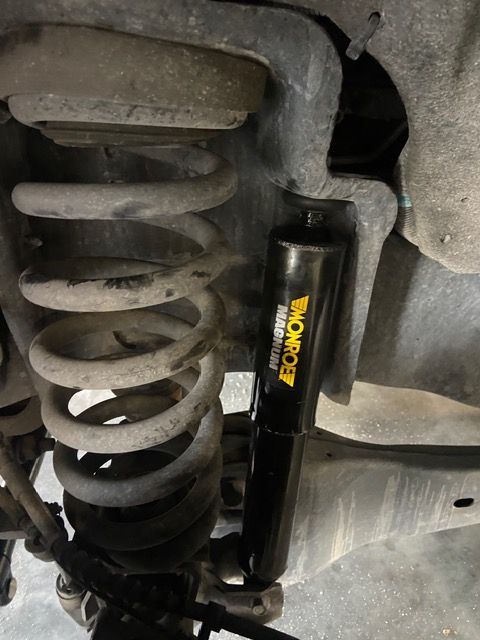 A vehicle's rear suspension, showing a Monroe shock absorber next to a coil spring, in a mechanic's shop.