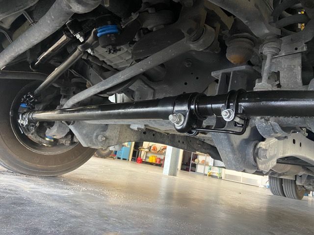 Undercarriage of a black vehicle, visible steering components and suspension, garage setting.