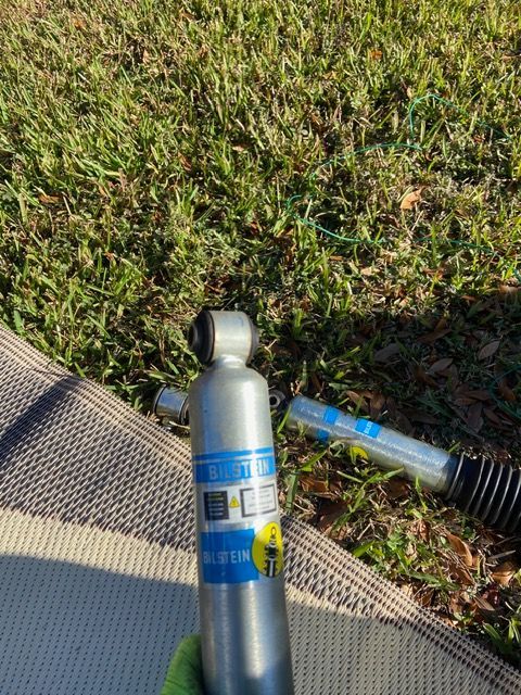 Two silver and blue Bilstein shock absorbers on a grassy surface.