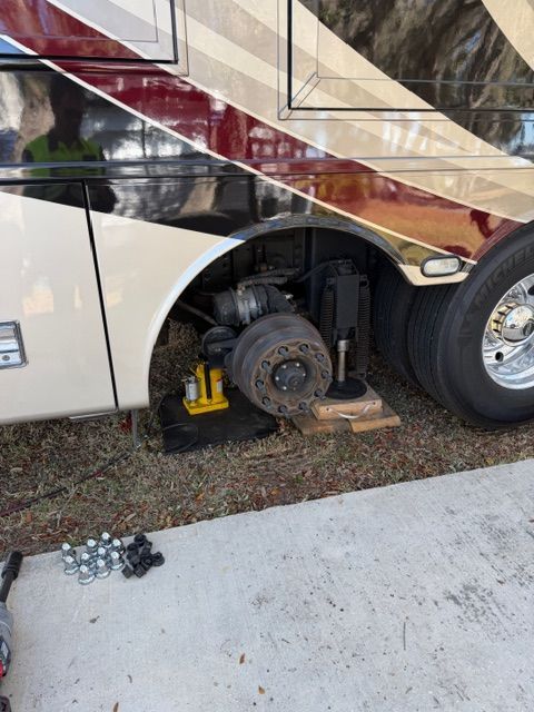 RV tire replacement: A coach is jacked up, wheel removed, tools and parts visible on the ground.