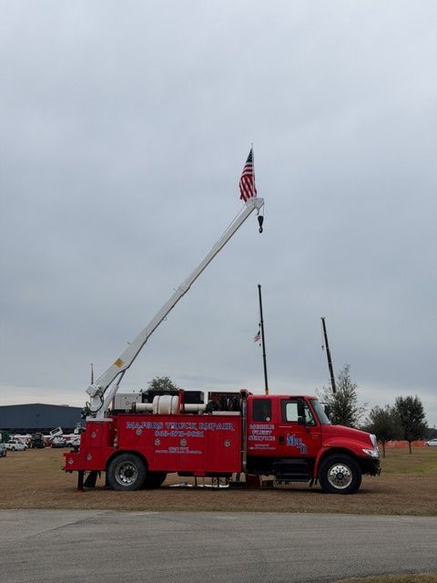 Red utility truck with a crane holding an American flag on a cloudy day.