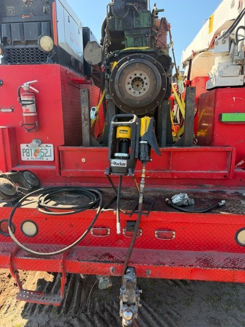 A partially disassembled heavy engine block secured on the bed of a red service truck with an attached power tool.