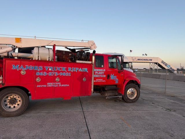 A red Majors Truck Repair service truck parked on a paved lot with a large structure in the background.