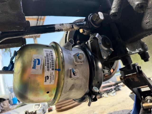A Bendix brake chamber mounted to a vehicle suspension assembly, with a jack stand visible underneath.