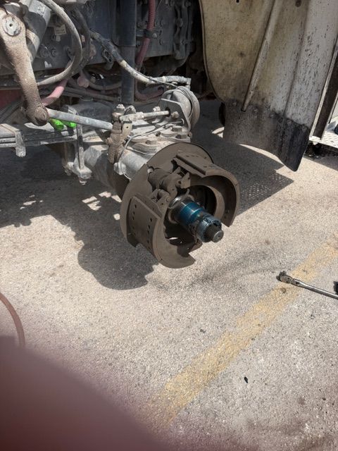 Close-up of a vehicle wheel hub and brake assembly being repaired on pavement.