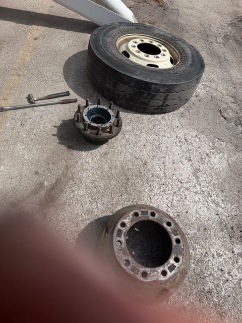 Car wheel parts on concrete: tire, hub assembly, and brake rotor, with a wrench nearby.