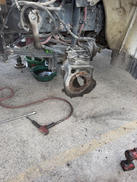 Vehicle engine removed and resting on the ground in a garage, with tools scattered nearby.