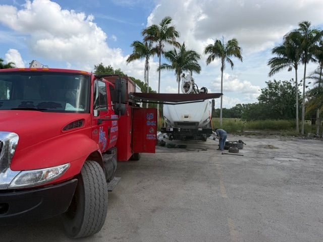 Red tow truck beside a white boat trailer in a palm-lined parking lot