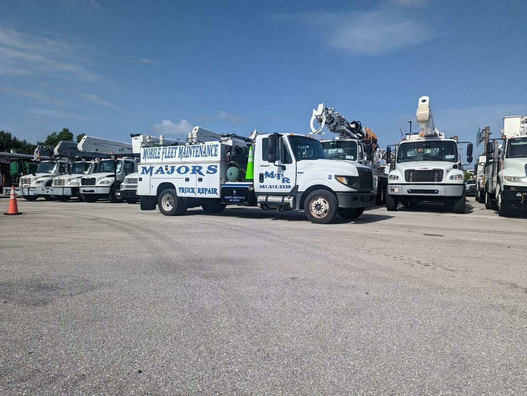 White work trucks with boom lifts parked in a gravel lot on a sunny day; some have company logos.