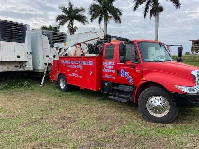 A red tow truck is parked in a grassy field next to a white trailer.