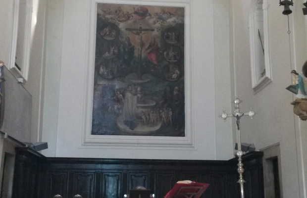 Grande dipinto religioso su una parete bianca all'interno di una chiesa; sotto è presente una pannellatura in legno scuro.