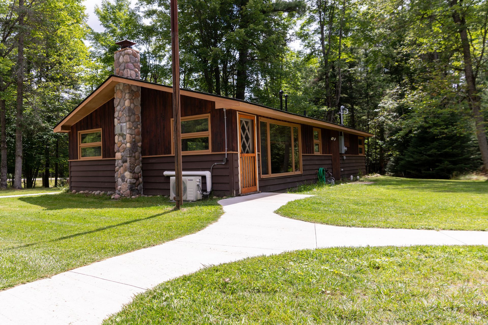 A log cabin with a stone chimney and a walkway leading to it.