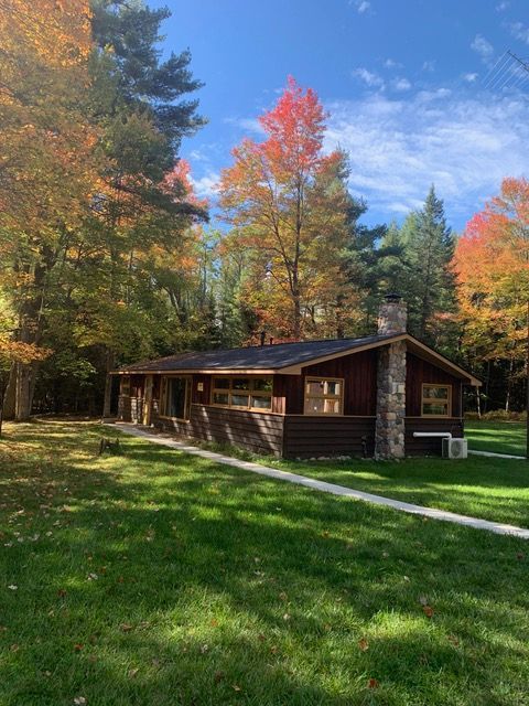 Cabin with a stone chimney surrounded by trees with autumn foliage on a sunny day.