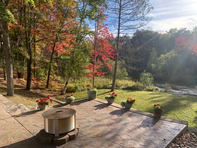 Patio overlooking a river, with red and green autumn trees and flower pots.