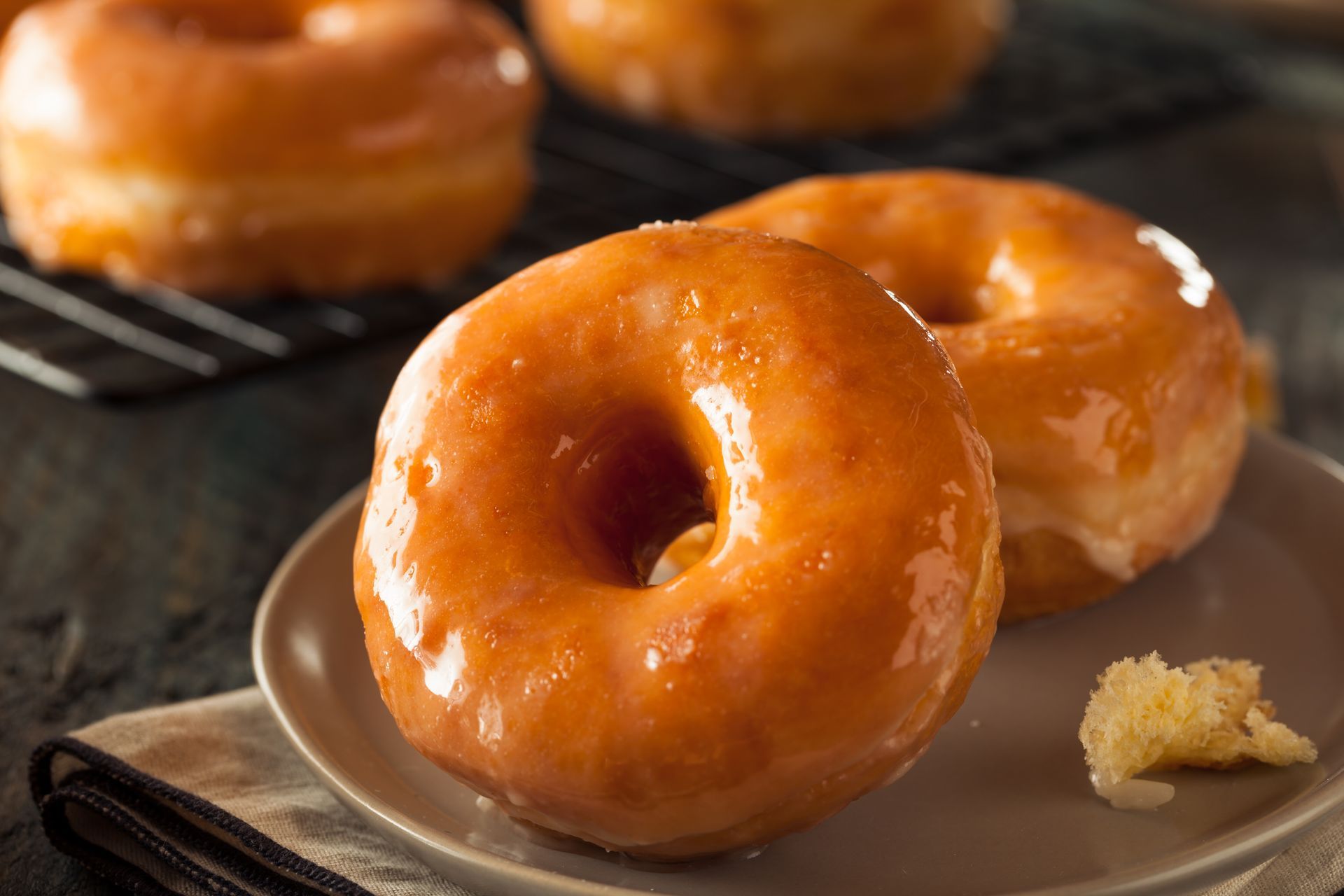 A close up of a plate of glazed donuts on a table.