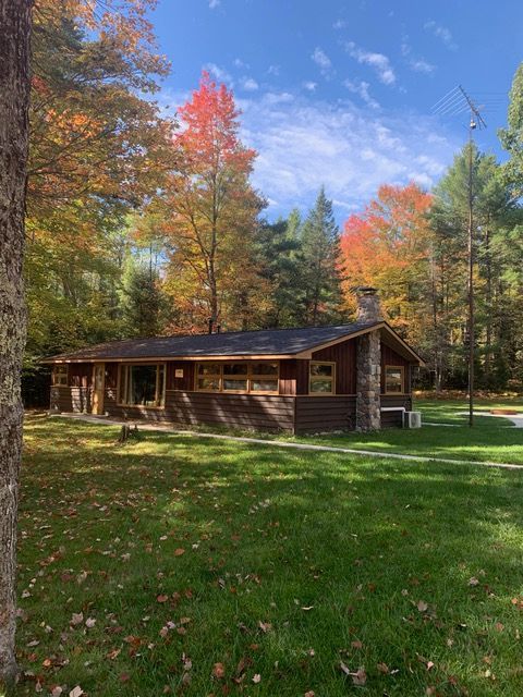 Cabin in autumn, surrounded by trees with vibrant red and orange leaves, on a sunny day.