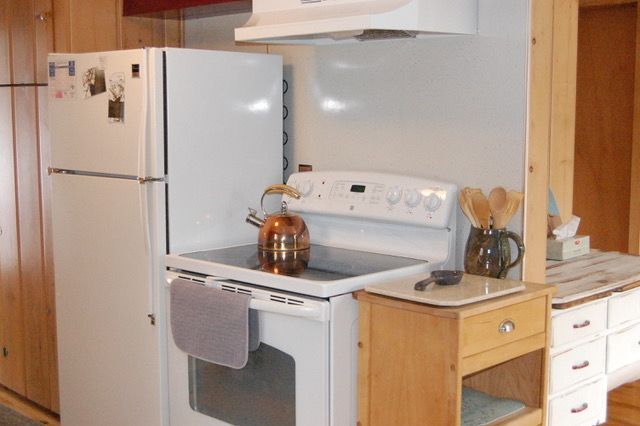 White kitchen appliances: refrigerator, stove with copper kettle, wooden cabinets.