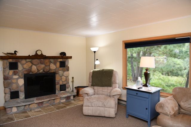 Cozy living room with stone fireplace, recliner, and blue side table near a window overlooking trees.