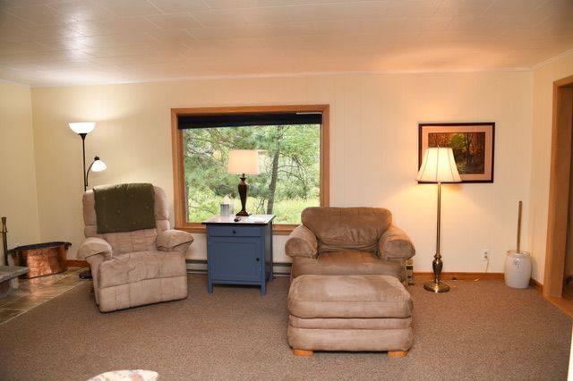Cozy living room with two armchairs, an ottoman, and a small blue table near a window with a view of trees.