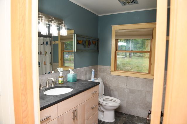 Bathroom with blue walls, beige vanity, toilet, and window with a view.