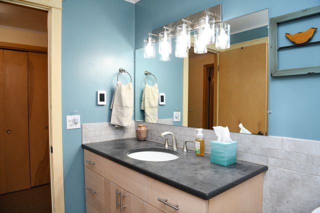 Bathroom with blue walls, light wood vanity, and a large mirror with a bright light fixture.