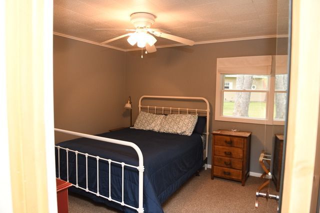 Bedroom with a white bed frame, dark blue bedding, brown nightstand, and gray walls.