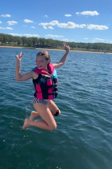 A girl wearing a life jacket is jumping into the water.