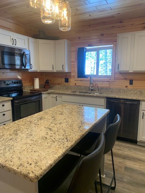 Kitchen with light-colored cabinets, granite countertops, and a wooden ceiling. An island with barstools.
