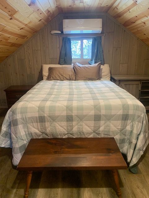 Bedroom with a bed, bench, wood paneling, and a window with curtains.