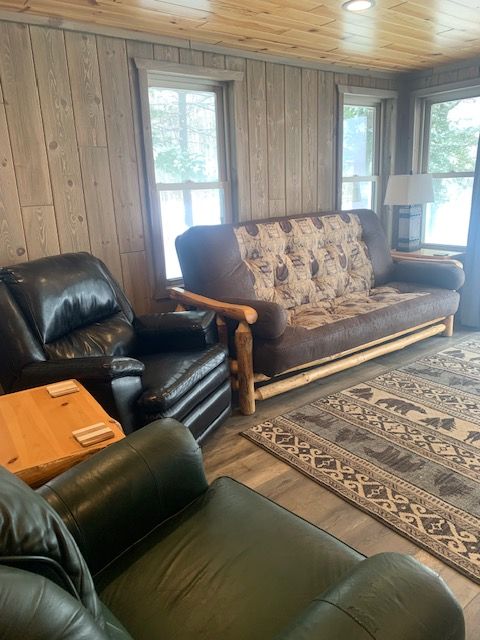 Living room with wood paneling, featuring leather chairs, a futon, and a rug with a bear pattern.