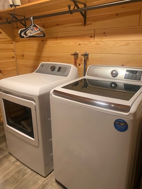 White washer and dryer in a laundry room with wood paneling. A clothes rack is above.