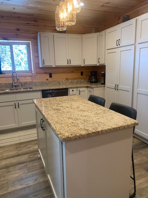 Kitchen with white cabinets, island with granite countertop, wood paneling, and a window.