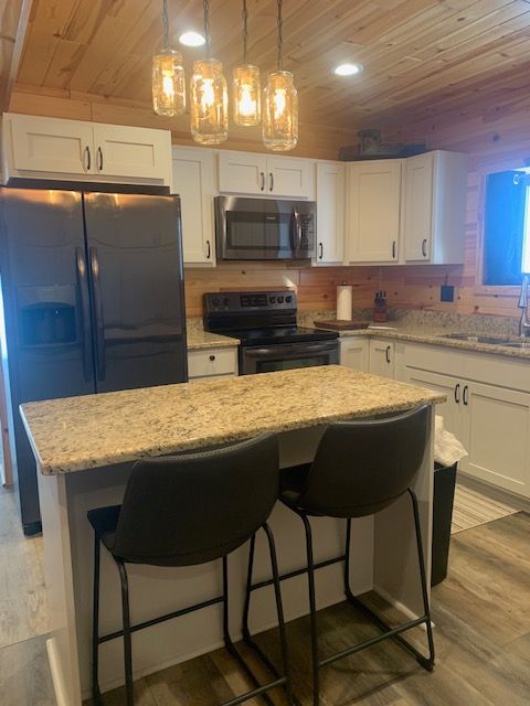 Kitchen with white cabinets, dark appliances, island with stools, and jar pendant lights.