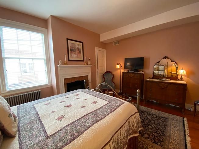 A bedroom with a bed , dresser , television and fireplace