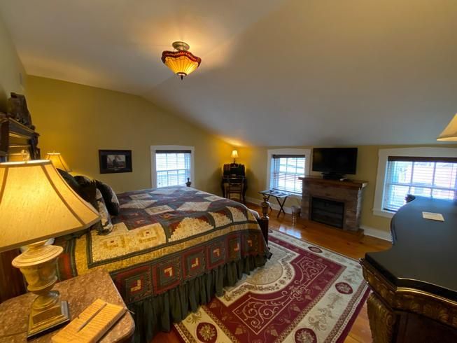 A bedroom with a large bed , lamps , a fireplace and a television.