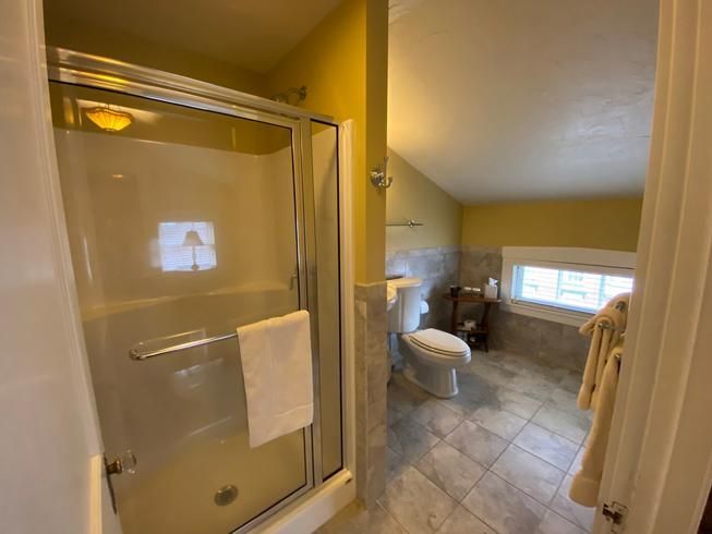 A bathroom with a toilet , sink , shower and window.