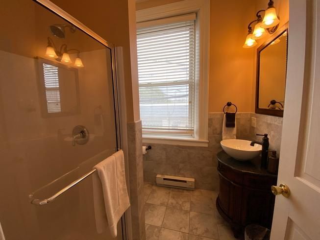 A bathroom with a sink , mirror , shower and window.