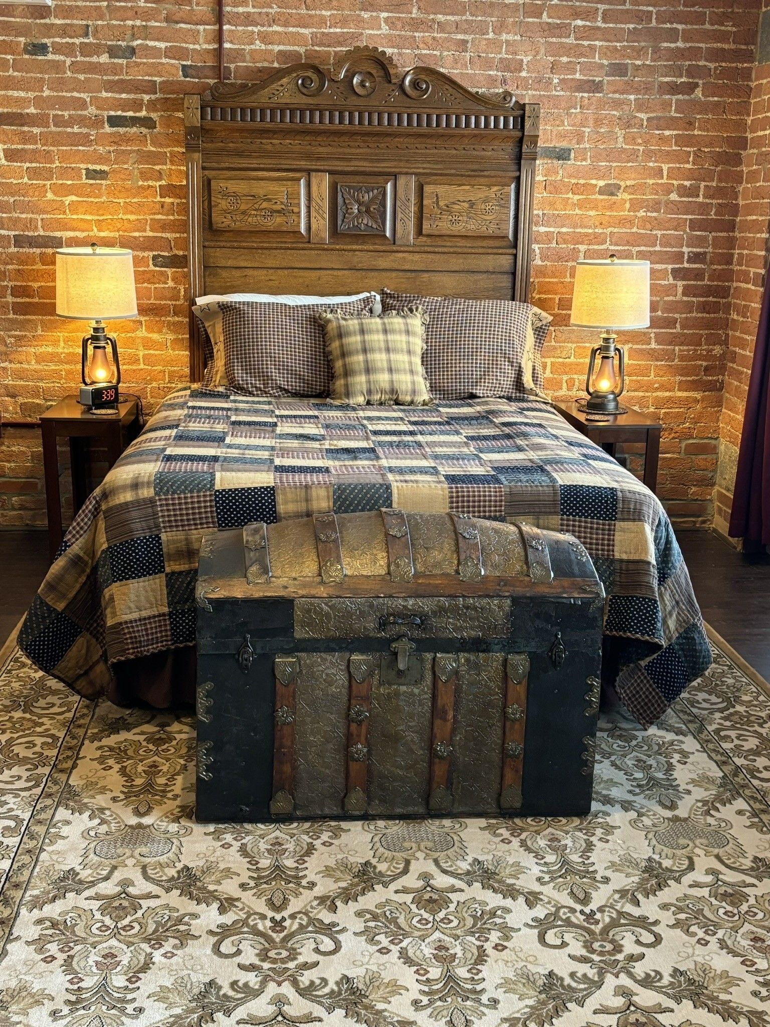 A bedroom with a bed , trunk , lamps and a brick wall.