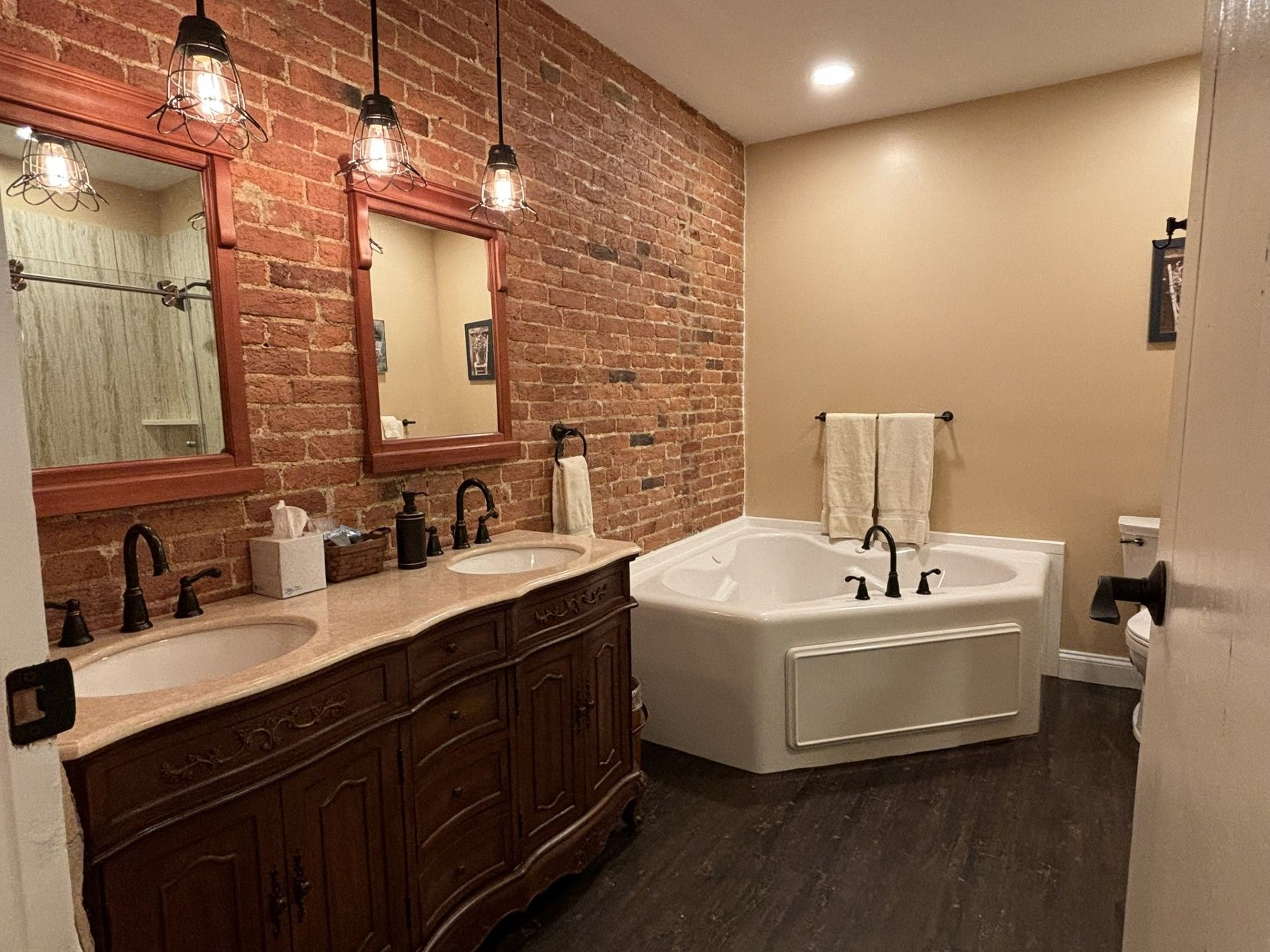 A bathroom with two sinks , a tub and a brick wall.