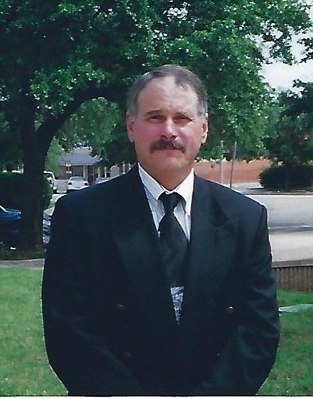 A man in a suit and tie stands in front of a tree