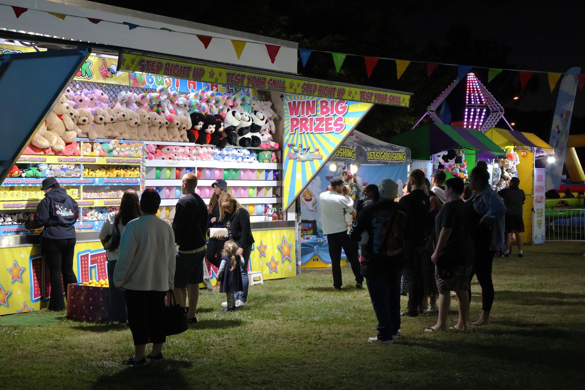 A Group Of People Are Standing In Front Of A Carnival Booth — Bills Amusements In Rockhampton, QLD
