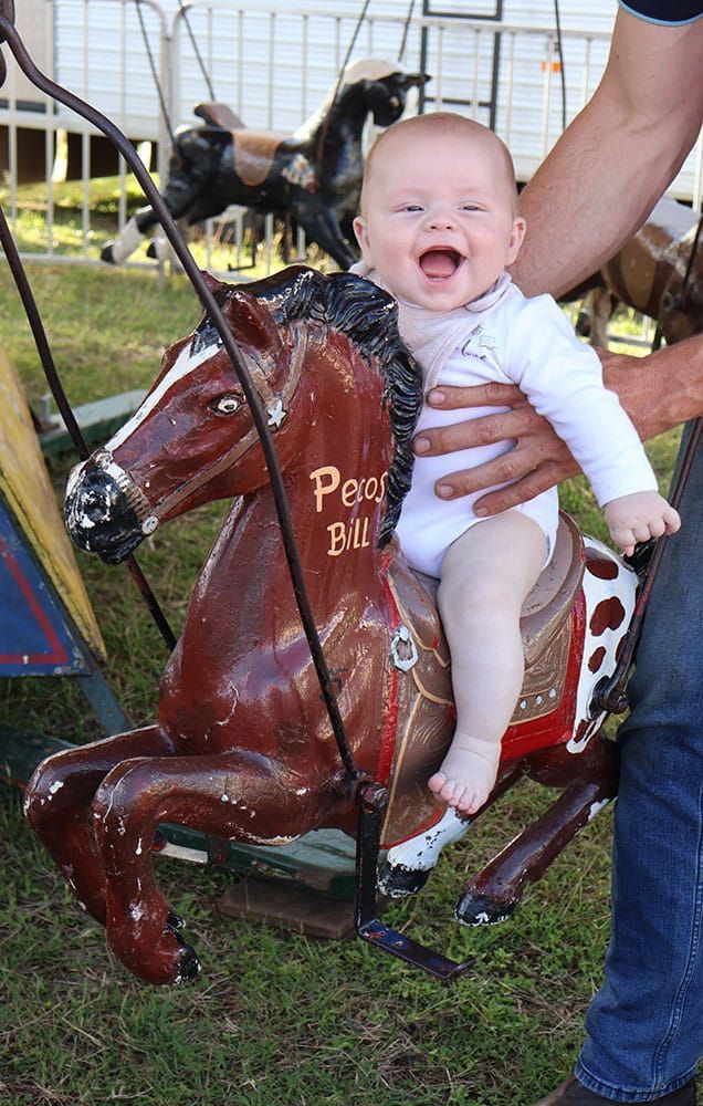 A Baby Is Sitting On A Rocking Horse And Smiling — Bills Amusements In Rockhampton, QLD