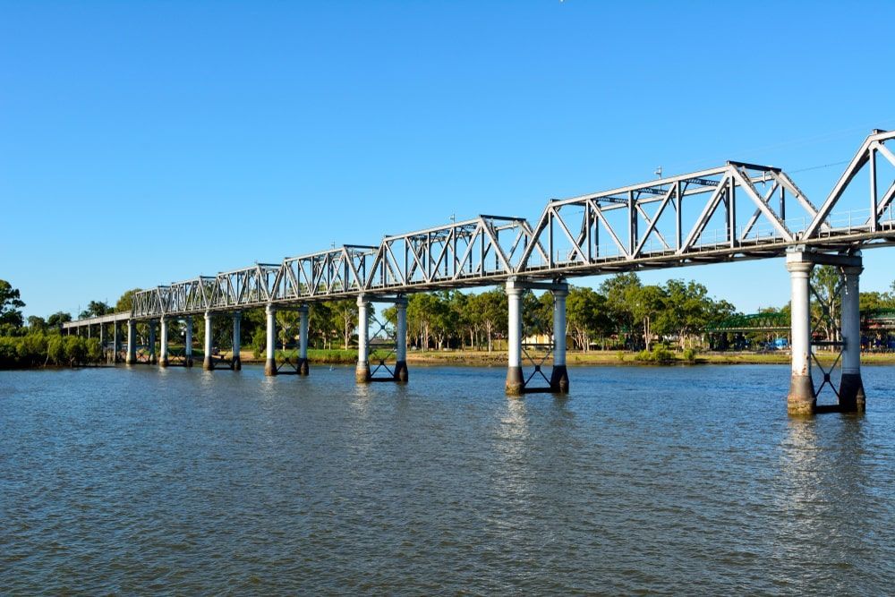 A Bridge Over A Body Of Water With Trees In The Background — Bills Amusements In Bundaberg, QLD