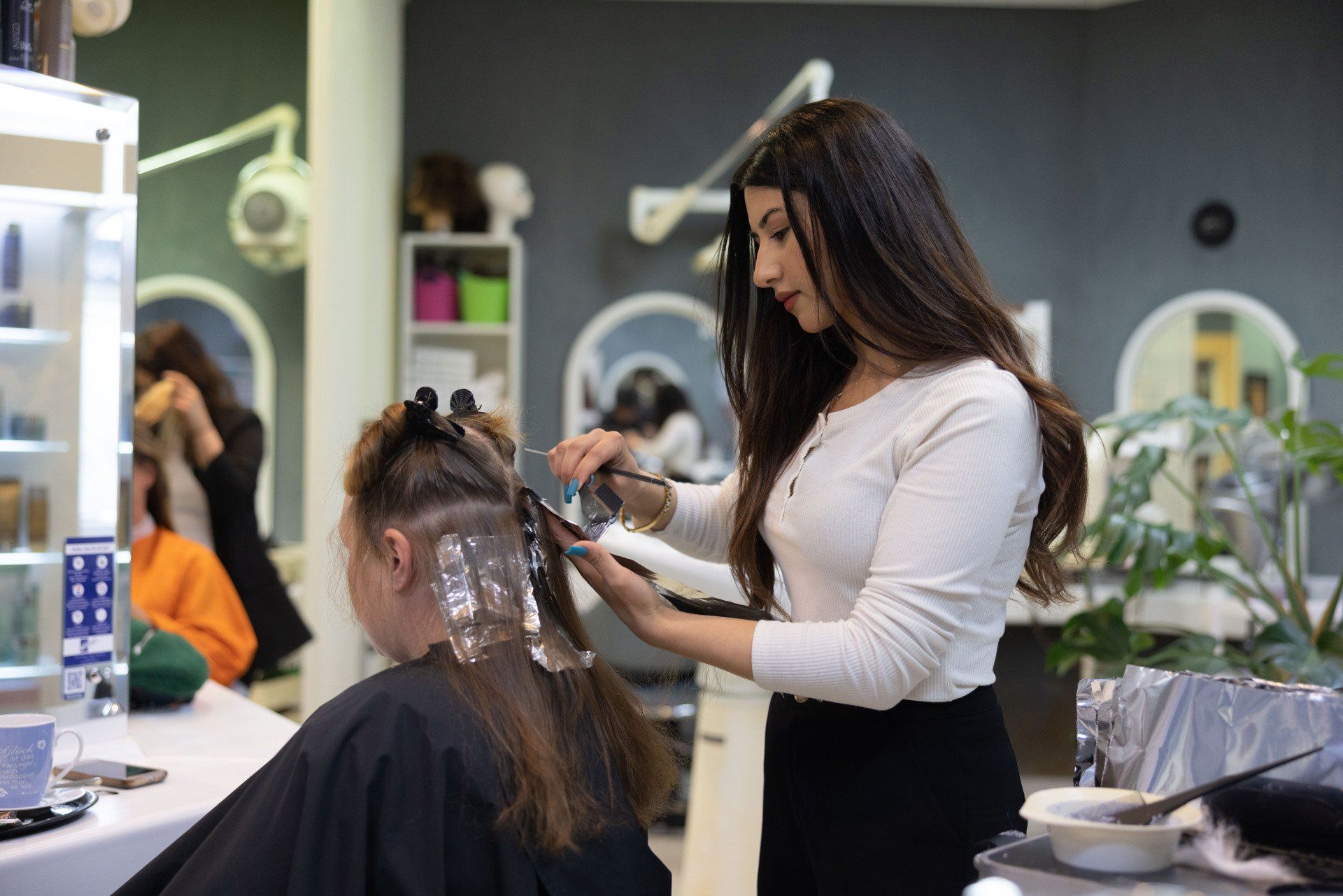 Friseur färbt Strähnchen ins Haar einer Kundin. Die Kundin sitzt.