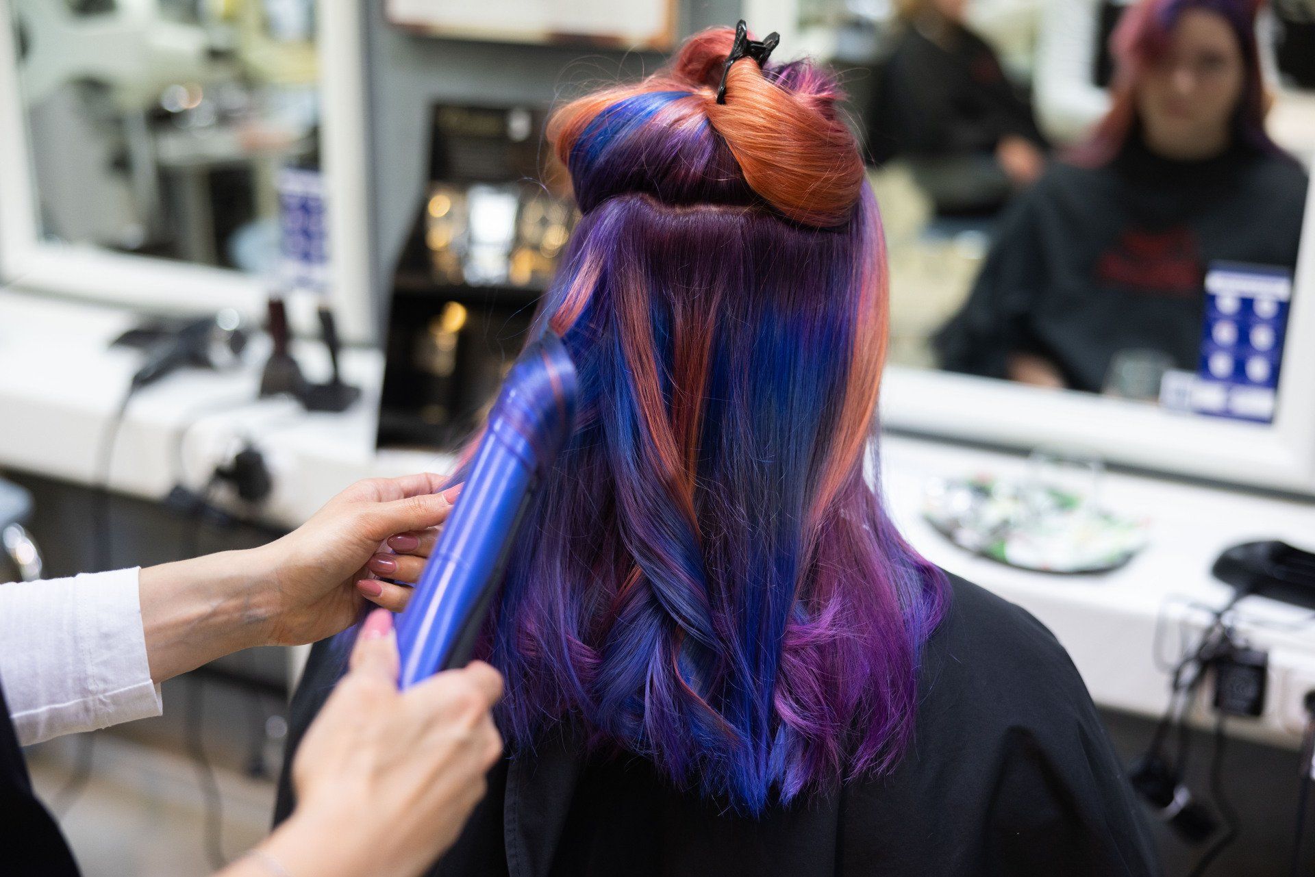 Person mit buntem Haar im Friseurstuhl, Friseur mit Glätteisen.