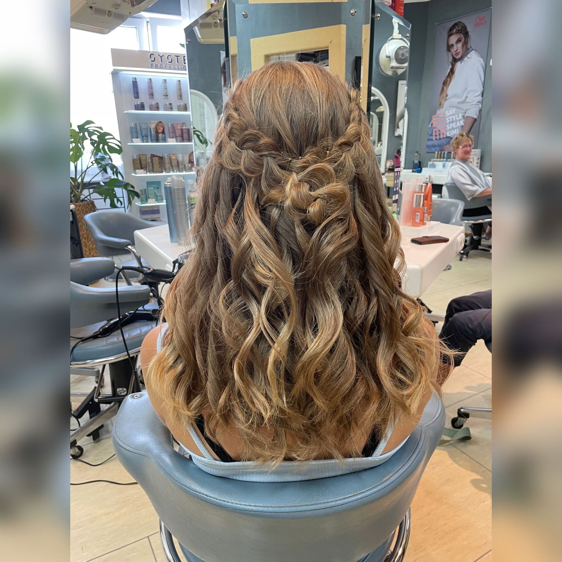 Frau mit welligem, hellbraunem Haar im Friseurstuhl, teilweise Hochsteckfrisur mit gedrehten Partien.