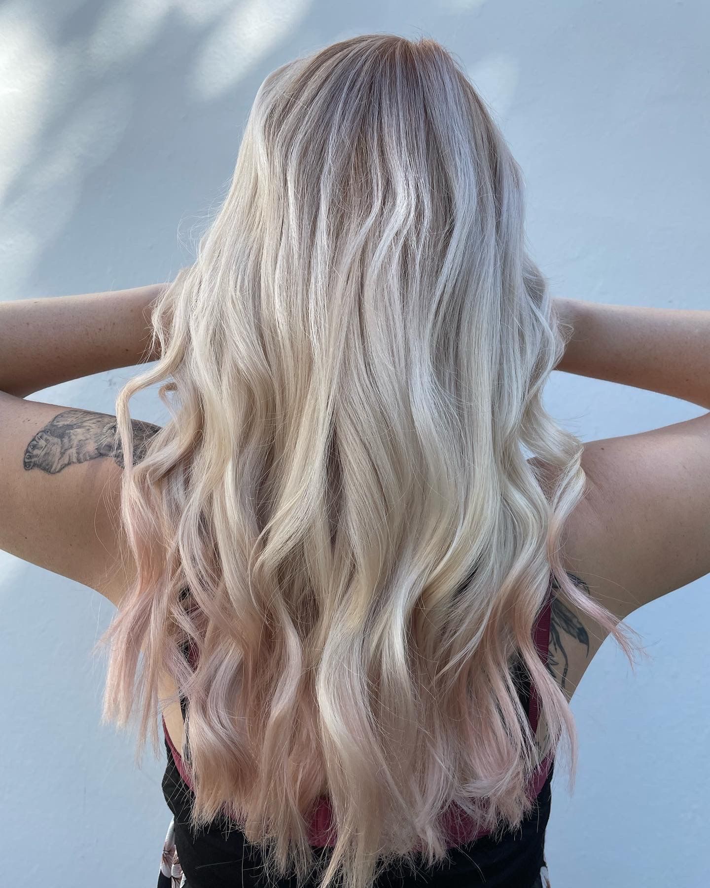 Frau mit langem, welligem, blondem Haar, das in rosa Spitzen übergeht, erhobenen Armen.