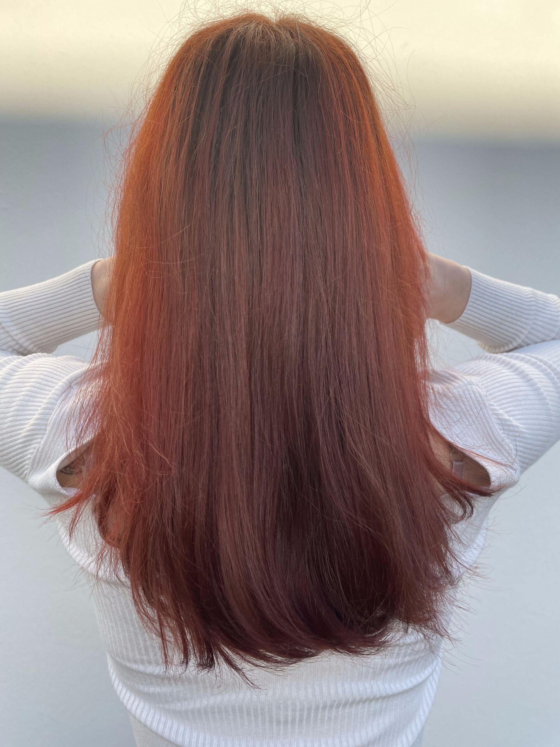 Frau mit langem, rotem, gewelltem Haar, erhobenen Armen und weißem Oberteil.